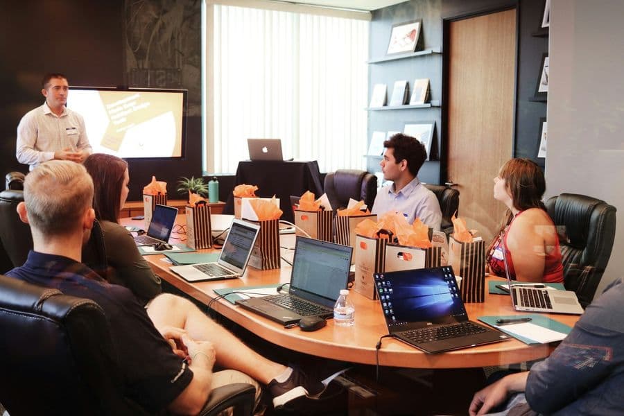 Facilitator leading a hands-on workshop as participants work on laptops around a conference table