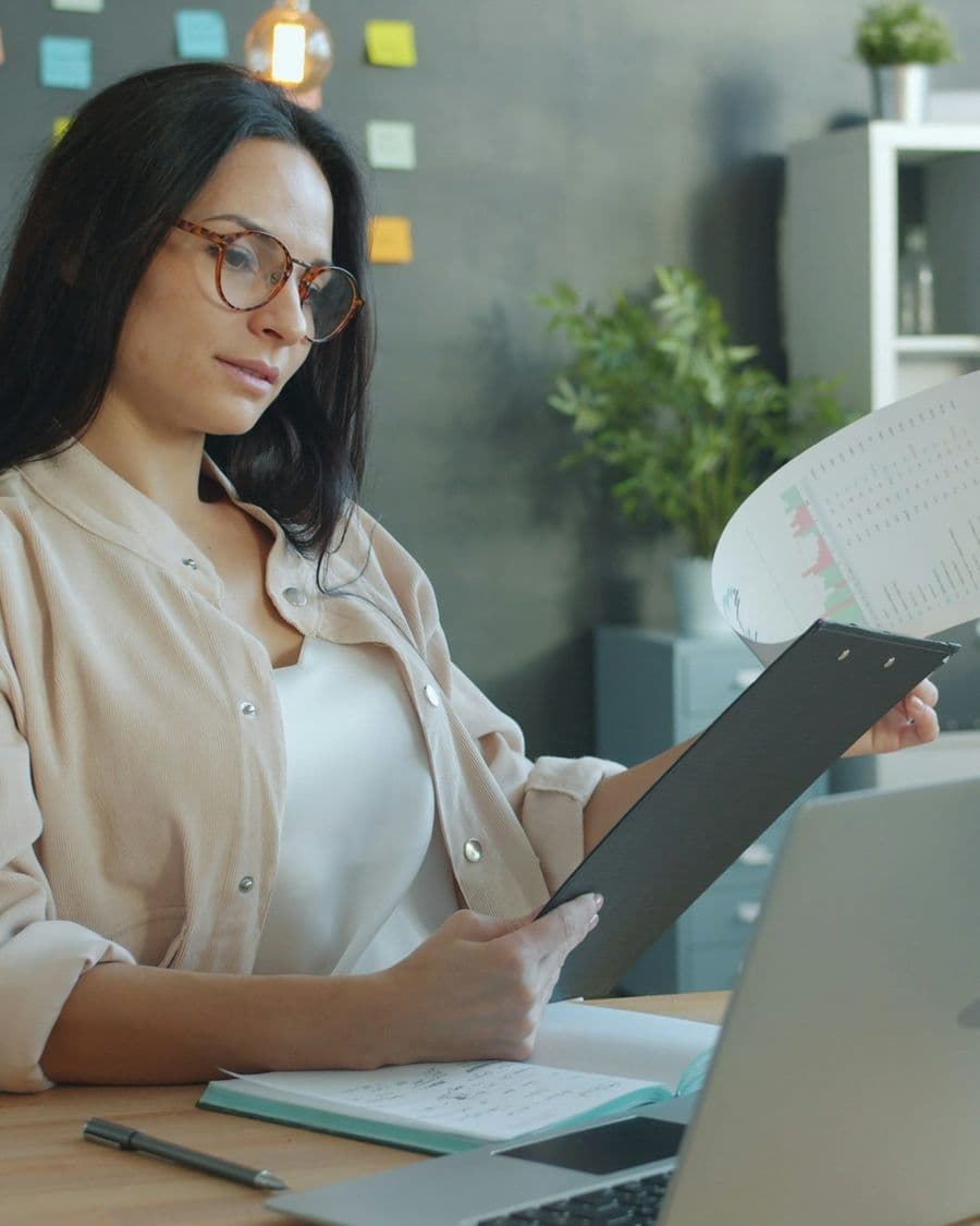 Finance analyst reviewing reports and charts at her desk