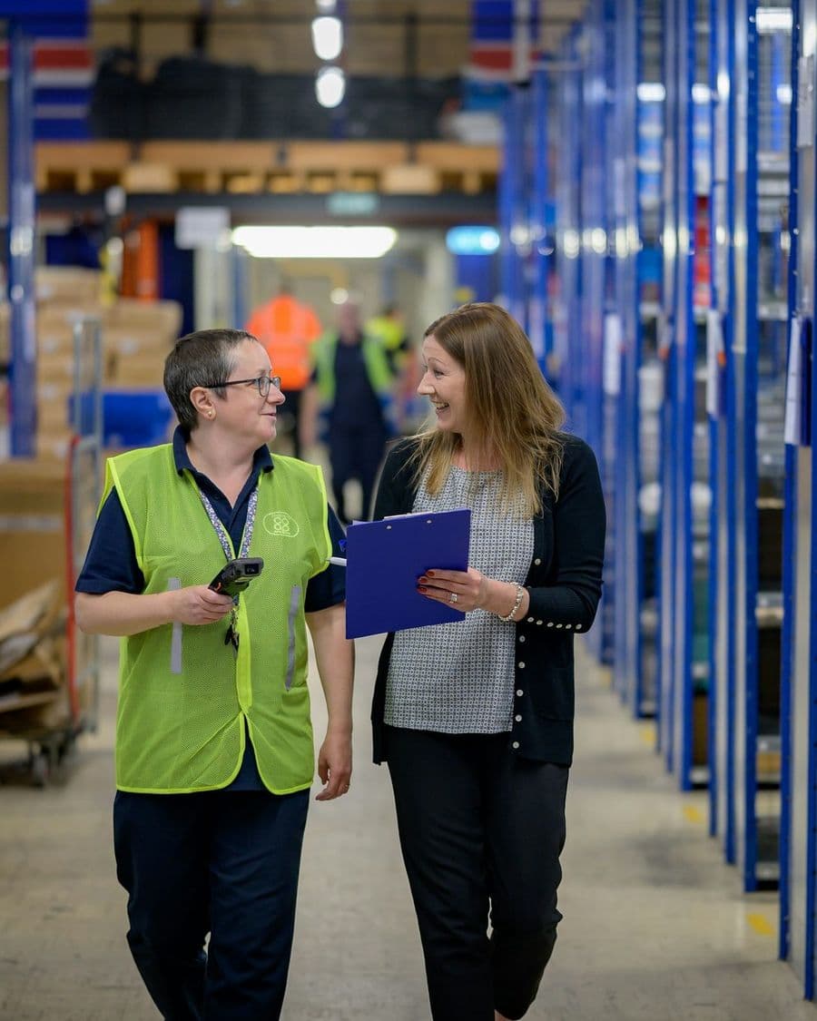Operations staff walking a warehouse aisle reviewing a clipboard