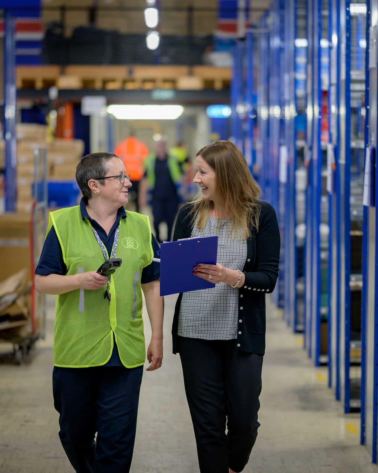 Operations staff walking a warehouse aisle reviewing a clipboard