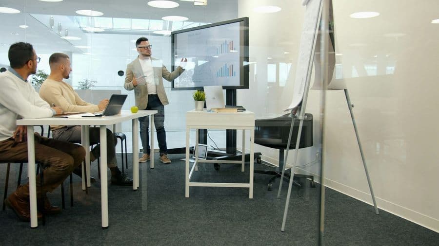 Facilitator presenting data on a large screen to a leadership team in a glass meeting room