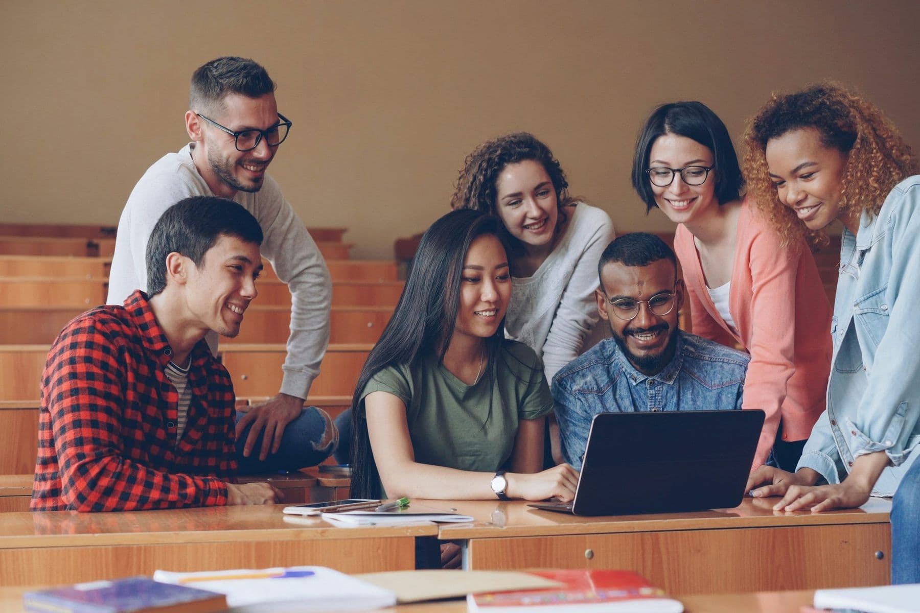 Diverse university students gathered around a laptop in a lecture hall